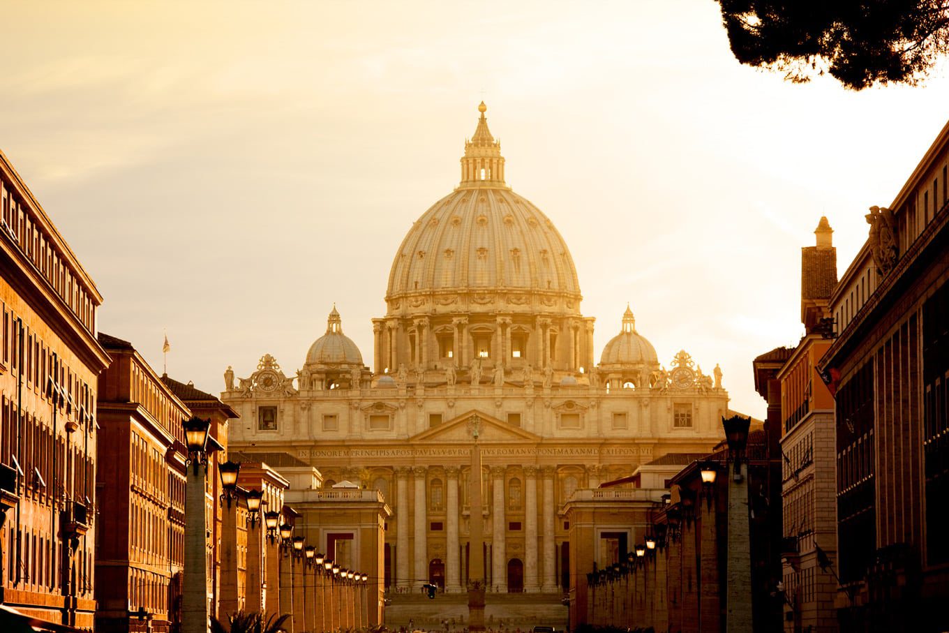 A imagem mostra a Basílica de São Pedro no Vaticano, capturada durante um pôr do sol que banha a construção em uma luz dourada suave.