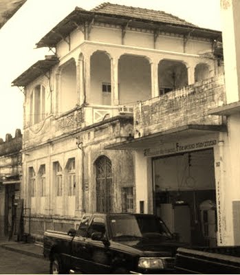 Imagem de um casarão, localizado em uma rua de Natal, RN, com uma caminhonete estacionada em frente.