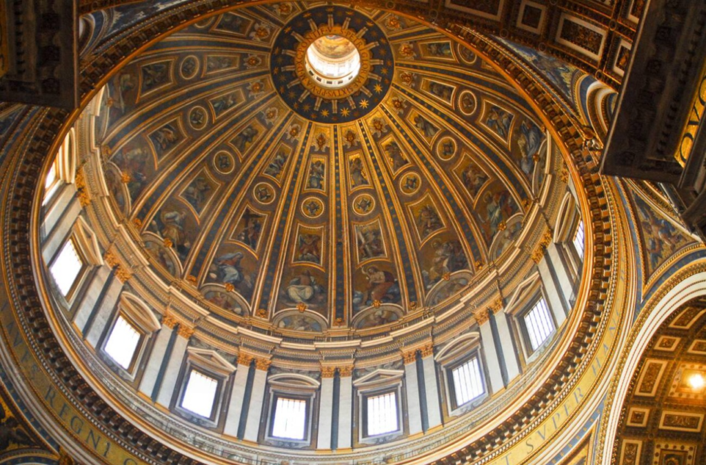 cúpula da Basílica de São Pedro, no Vaticano, uma das maiores obras da arquitetura renascentista. O design, concluído por Michelangelo, é ricamente decorado com afrescos e detalhes dourados que capturam cenas religiosas, acompanhadas por uma inscrição em latim ao redor de sua base. As janelas deixam a luz natural iluminar o interior, destacando a beleza das formas arquitetônicas e artísticas.