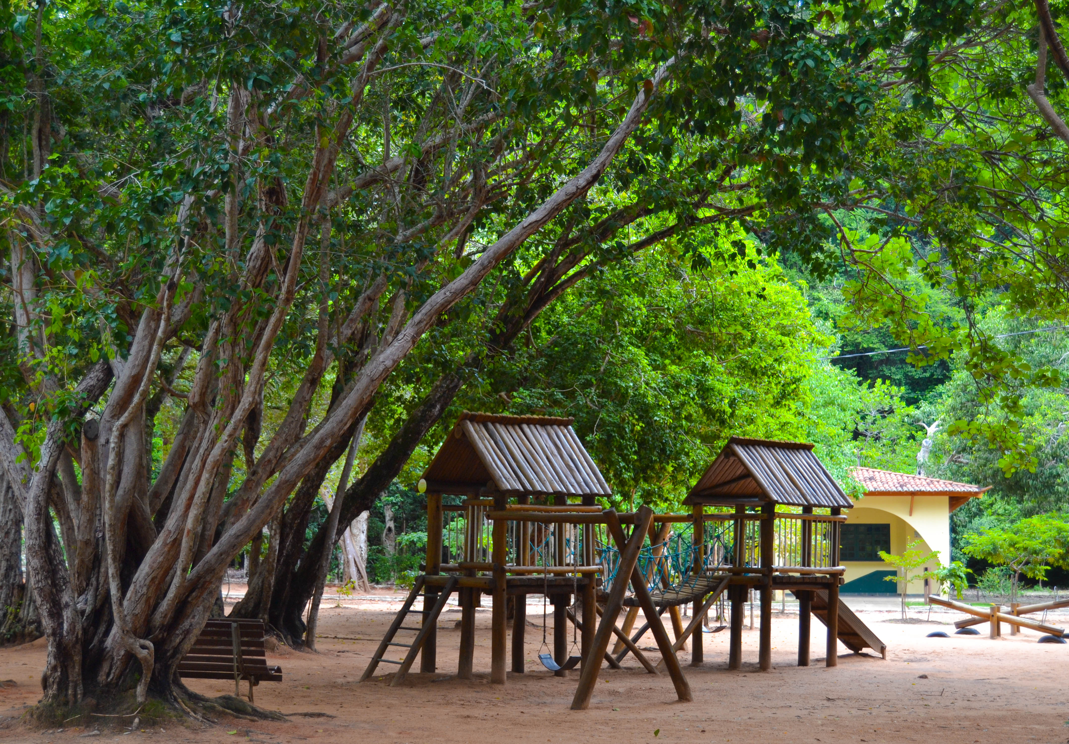 Parque infantil no meio da natureza no Parque Estadual Dunas de Natal. A imagem mostra estruturas de madeira para recreação cercadas por árvores frondosas, criando um ambiente natural e tranquilo. Ótimo local para lazer em meio à natureza.