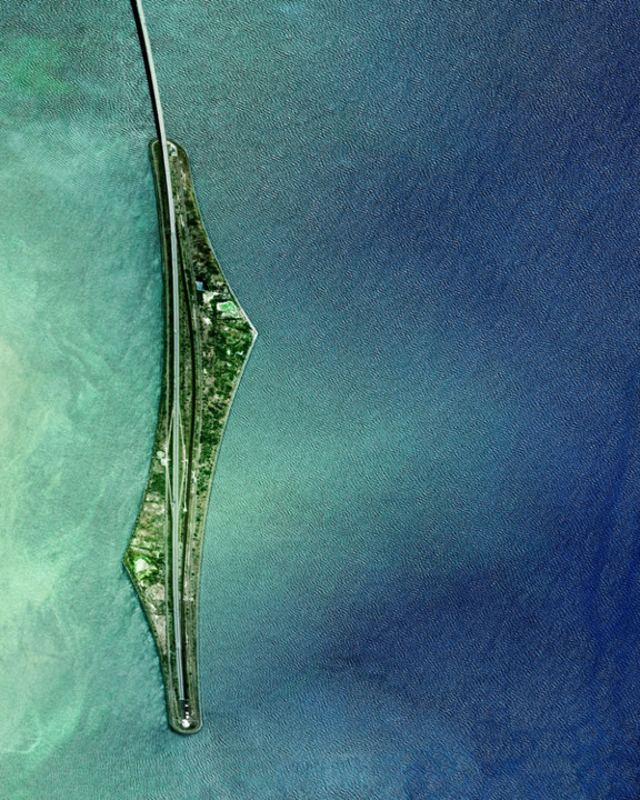 Vista aérea da ilha artificial de Peberholm, construída para a Ponte Oresund, que conecta a Dinamarca e a Suécia. A ilha, com formato alongado, abriga a transição entre o túnel subaquático e a ponte suspensa, além de ser um habitat para diversas espécies de plantas e animais. Peberholm é um exemplo de projeto sustentável, combinando engenharia e preservação ambiental.