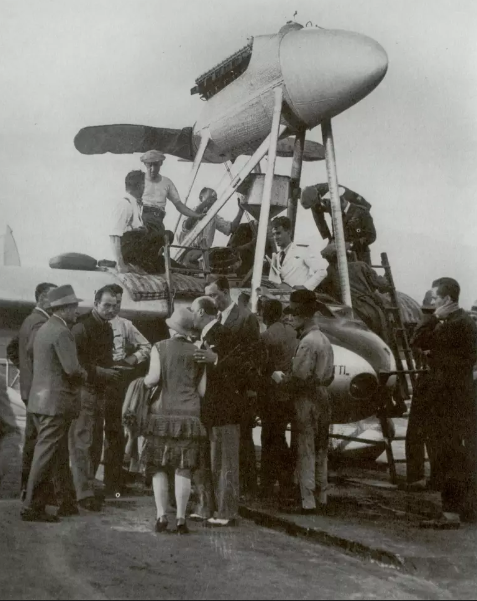 Imagem histórica do voo Roma-Natal em 1928, com aviadores e equipe ao redor da aeronave. Evento marcou a relação entre Itália e Brasil.