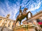 A icônica estátua equestre de Marco Aurélio na Piazza del Campidoglio, com o imponente Palazzo Senatorio ao fundo e o céu azul em contraste. A cena reflete a harmonia renascentista projetada por Michelangelo, combinando arquitetura, história e arte em um dos locais mais emblemáticos de Roma.