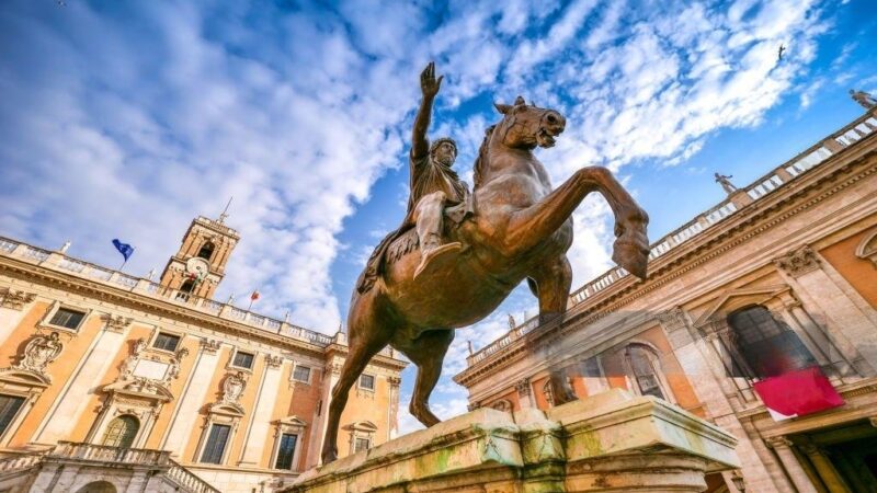 A icônica estátua equestre de Marco Aurélio na Piazza del Campidoglio, com o imponente Palazzo Senatorio ao fundo e o céu azul em contraste. A cena reflete a harmonia renascentista projetada por Michelangelo, combinando arquitetura, história e arte em um dos locais mais emblemáticos de Roma.