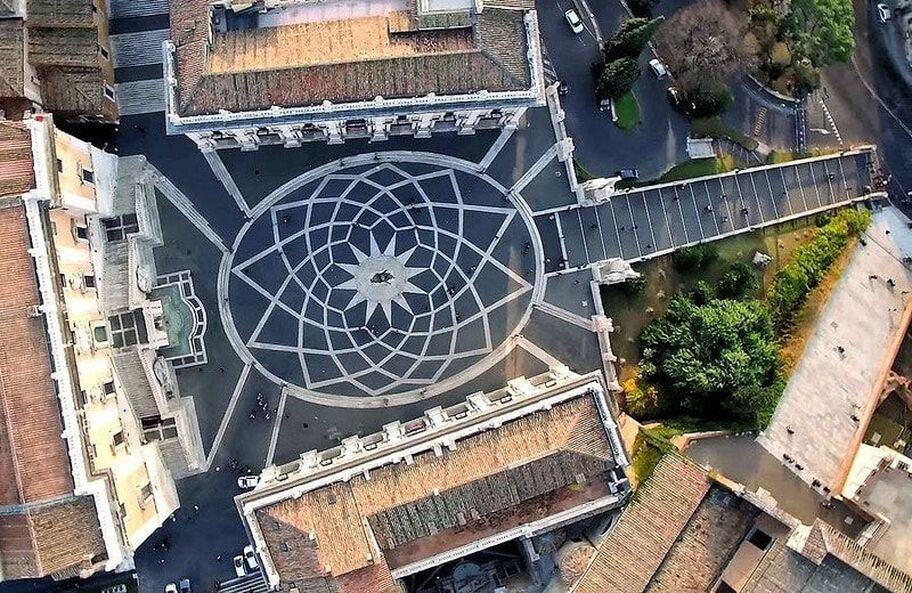 Vista aérea da Piazza del Campidoglio, destacando o desenho geométrico do pavimento projetado por Michelangelo, com uma estrela central rodeada por linhas harmoniosas. A simetria dos edifícios renascentistas realça a beleza arquitetônica do local.