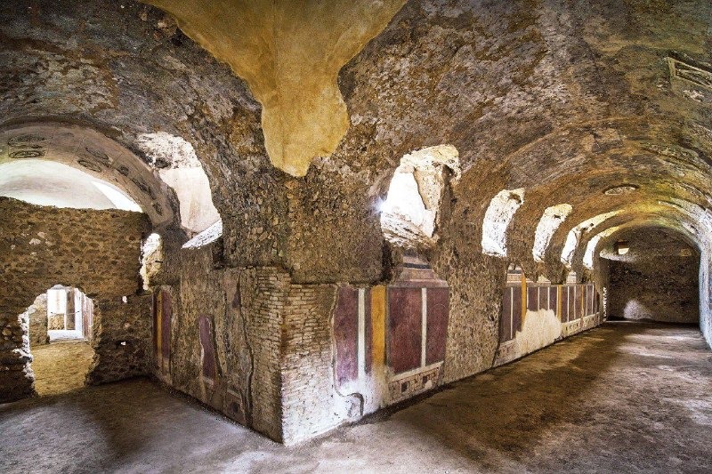 Interior de uma estrutura subterrânea romana em Pompeia, com arcos decorativos e paredes pintadas com afrescos coloridos, preservando detalhes da arquitetura antiga.