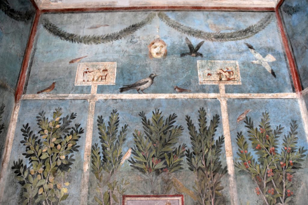 Detalhe de um afresco romano em Pompeia, retratando cenas com pássaros, vegetação e elementos simbólicos, preservando a arte decorativa da Antiguidade.
