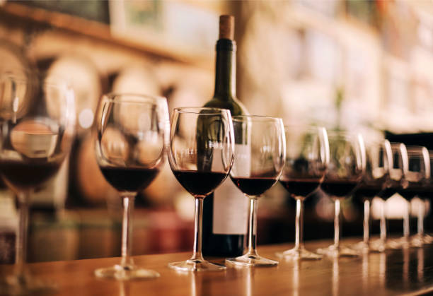 Vinhos servidos em taças alinhadas em uma mesa de bar, com um frasco de vinho ao fundo, criando uma atmosfera elegante e convidativa.