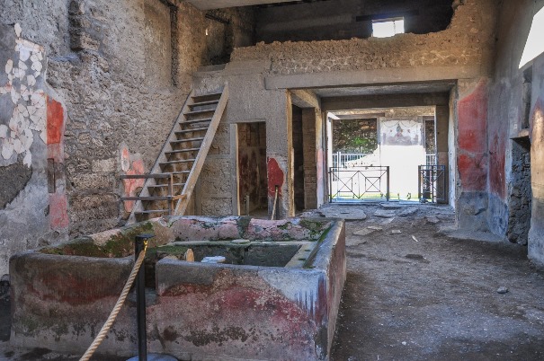 Interior de uma casa romana em Pompeia, com escadaria de pedra e afrescos nas paredes, destacando detalhes arquitetônicos preservados.